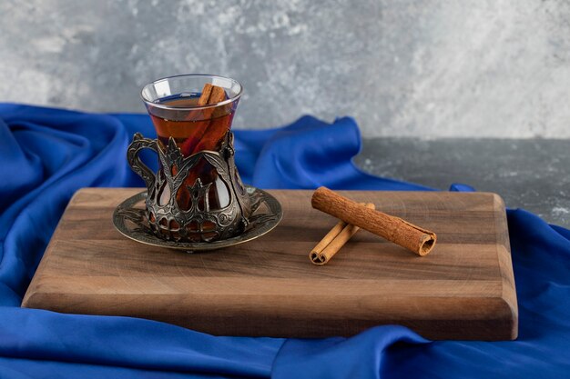 Un té de cristal con canela en rama sobre una tabla de cortar de madera.