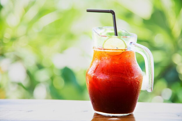 Té helado en la mesa de madera sobre jardín verde - relájese con una bebida en concepto de naturaleza