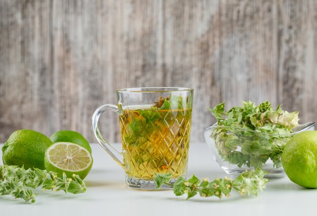 Té de hierbas con hierbas, limas en una taza de vidrio en blanco y sucio,