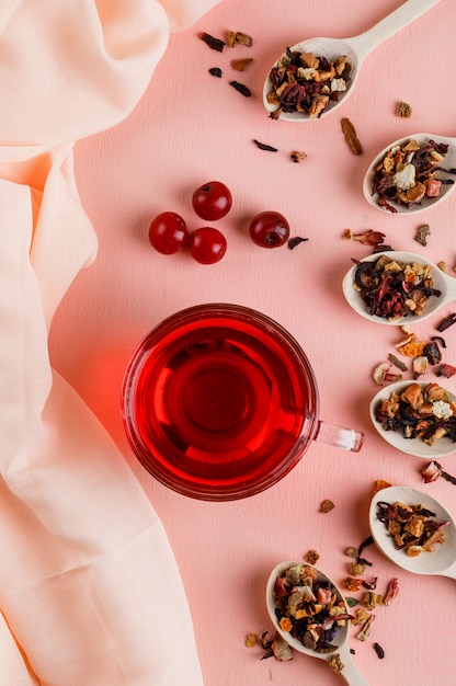 Té con hierbas secas, cerezas en una taza de vidrio en rosa y textil.