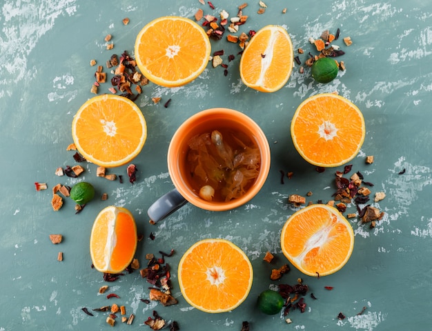 Foto gratuita té con hierbas secas mixtas, naranjas, limas en una taza sobre la superficie de yeso