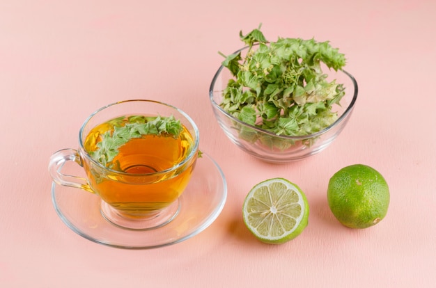 Té de hierbas en una taza de vidrio con hierbas, limas alto ángulo de visión en una rosa