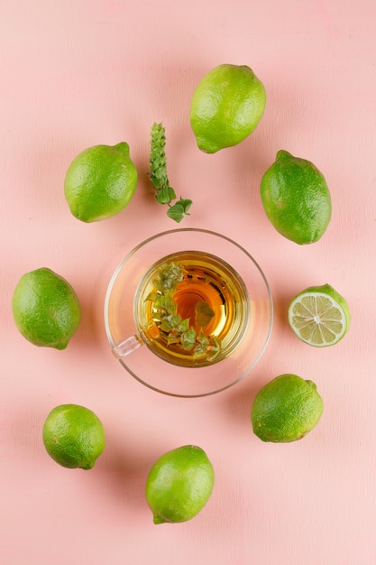 Té de hierbas en una taza de vidrio con hierbas, limas vista superior en una rosa