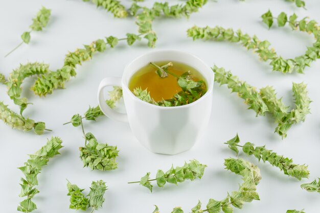 Té de hierbas en una taza con vista de ángulo alto de hojas sobre un blanco