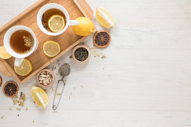 Té de limón con limones en bandeja y hierbas en mesa de madera blanca