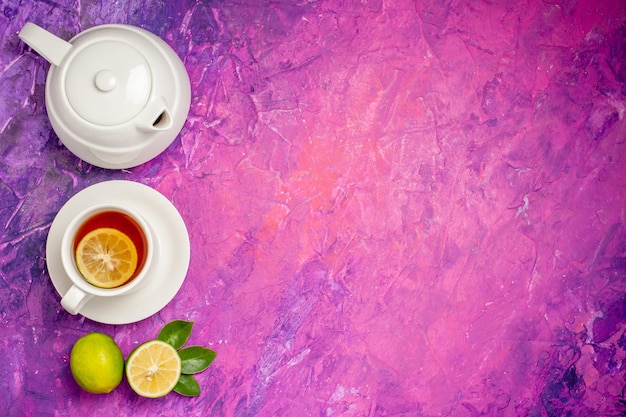 Foto gratuita té con limón una taza de té con limón al lado de la tetera y limas en el lado izquierdo de la mesa rosa-violeta