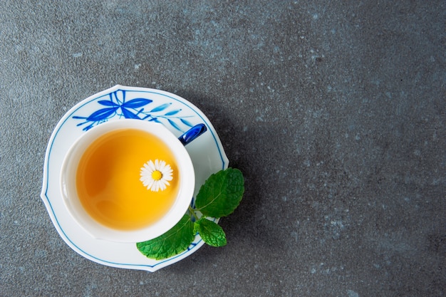 Té de manzanilla orgánica en una taza y platillo con hojas verdes vista superior sobre un fondo de estuco gris