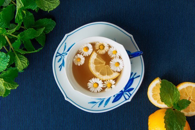 Té de manzanilla saludable con limones y hojas en una taza y salsa sobre fondo oscuro mantel, primer plano.