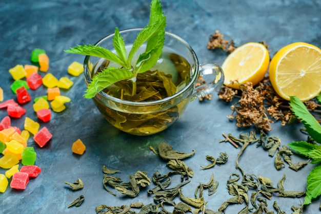 Foto gratuita té con menta, hierbas secas, limón, dulces en una taza sobre la superficie azul oscuro, vista de ángulo alto.