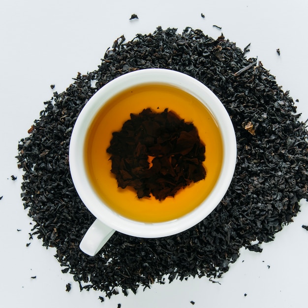 Té negro en una taza y hojas secas sobre fondo blanco.