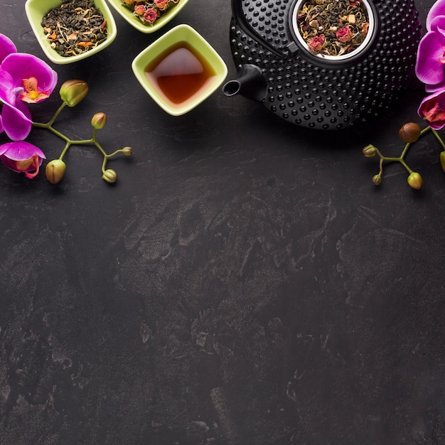 Té saludable con ingrediente seco y flor de orquídea rosa sobre fondo negro