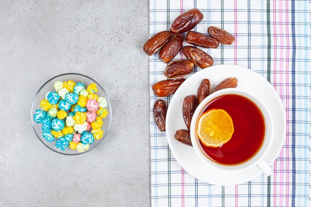 Té en taza blanca con dátiles y un tazón de dulces sobre fondo de mármol. Foto de alta calidad