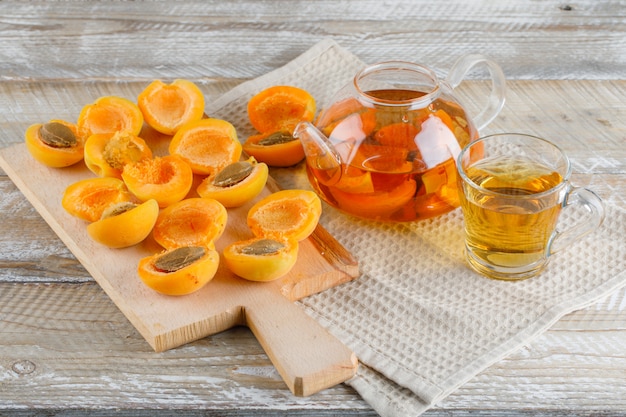 Té en tetera y taza con albaricoques, vista superior de tabla de cortar en madera y papel de cocina