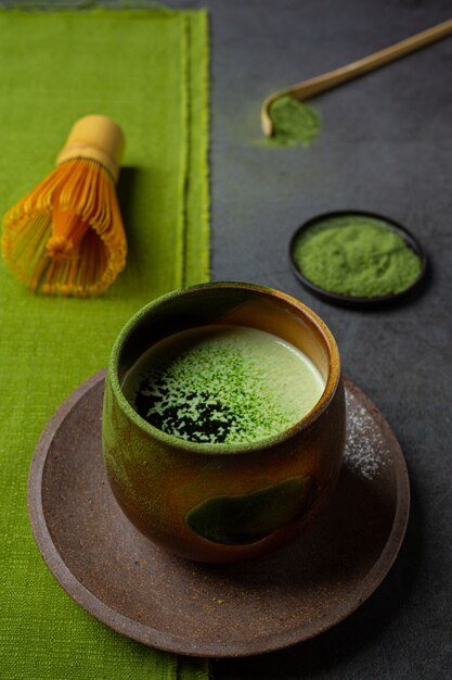 Té verde caliente en un vaso con crema cubierto con té verde, decorado con té verde en polvo.