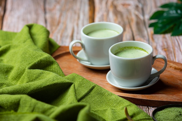 Té verde caliente en un vaso con crema cubierto con té verde, decorado con té verde en polvo.