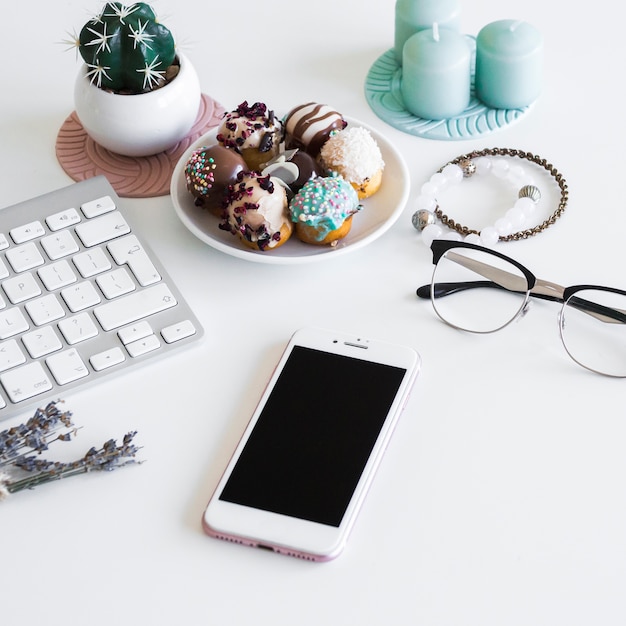 Teclado cerca de smartphone, velas, gafas y galletas en plato