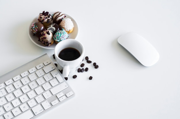 Teclado cerca de taza, galletas y ratón de ordenador.