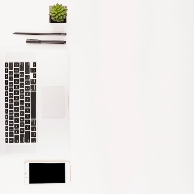 Teclado portátil; Teléfono móvil; planta en maceta; pluma y lápiz sobre fondo blanco