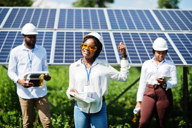 Técnico afroamericano verifica el mantenimiento de los paneles solares Grupo de tres ingenieros negros reunidos en la estación solar