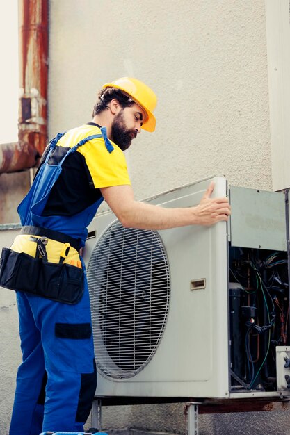 Técnico certificado contratado para arreglar el aire acondicionado roto, desmantelando el panel de la bobina delantera del condensador para comprobar los componentes internos defectuosos.