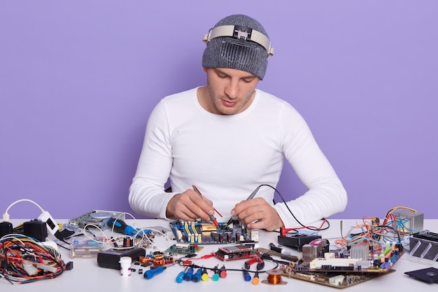 Técnico concentrado que repara el interior del teléfono inteligente o la computadora portátil con un multímetro en el laboratorio