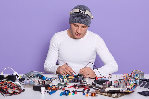 Técnico concentrado que repara el interior del teléfono inteligente o la computadora portátil con un multímetro en el laboratorio