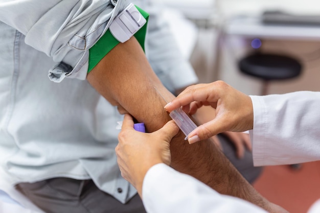 Técnico de flebotomía joven y especializado que aplica un torniquete al brazo de un paciente masculino para la punción venosa