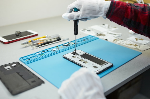 Foto gratuita técnico en guantes antiestáticos con destornillador para desmontar el teléfono móvil borken, ir a reparar la placa base, sentarse en su lugar de trabajo en el laboratorio con el equipo necesario