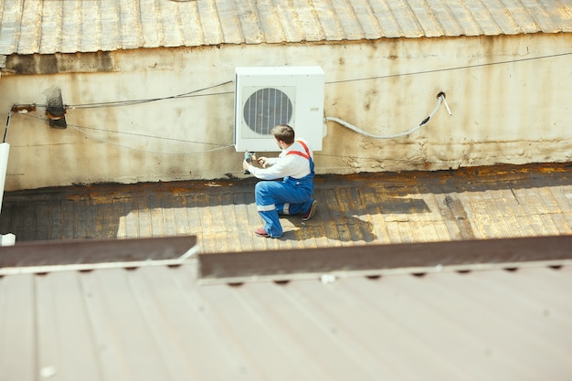 Técnico de HVAC trabajando en una parte del condensador para la unidad de condensación. Trabajador o reparador de sexo masculino en uniforme reparando y ajustando el sistema de acondicionamiento, diagnosticando y buscando problemas técnicos.