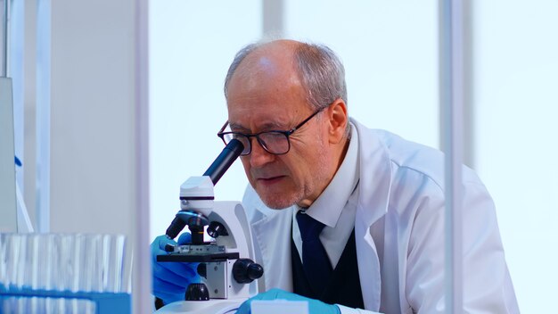 Técnico de laboratorio senior examinando muestras y líquidos con microscopio en laboratorio equipado. Científico que trabaja con diversas bacterias, tejidos y muestras de sangre, investigación farmacéutica de antibióticos