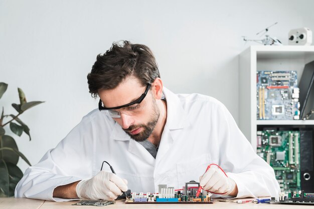 Técnico masculino que examina la computadora rota con multímetro digital