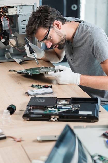 Foto gratuita técnico masculino que repara la placa madre del ordenador en el escritorio de madera