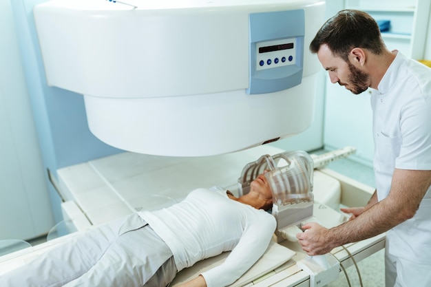 Técnico médico preparando a su paciente que se somete a un examen de resonancia magnética cerebral en el hospital