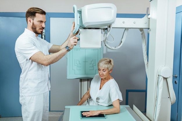 Técnico médico que inicia la exploración de rayos X de la mano de un paciente maduro en la clínica médica