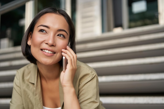 Tecnología celular sonriente niña asiática habla por teléfono móvil hace una llamada mujer joven con teléfono