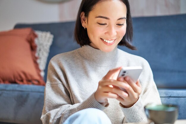 Tecnología y gente joven mujer asiática con estilo se sienta en casa con su teléfono inteligente mensaje de texto usi