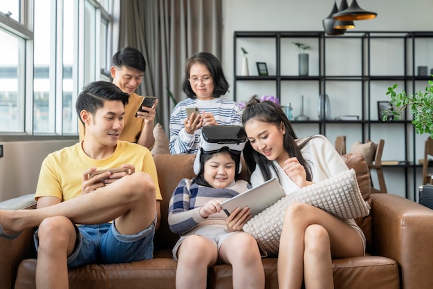 Tecnología inteligente con estilo de vida en el hogar. La familia de la generación asiática disfruta del dispositivo de tecnología. Usa la tableta del teléfono inteligente y las gafas de gafas vr para divertirse juntos en el sofá de la sala de estar en el momento de cuarentena en casa.