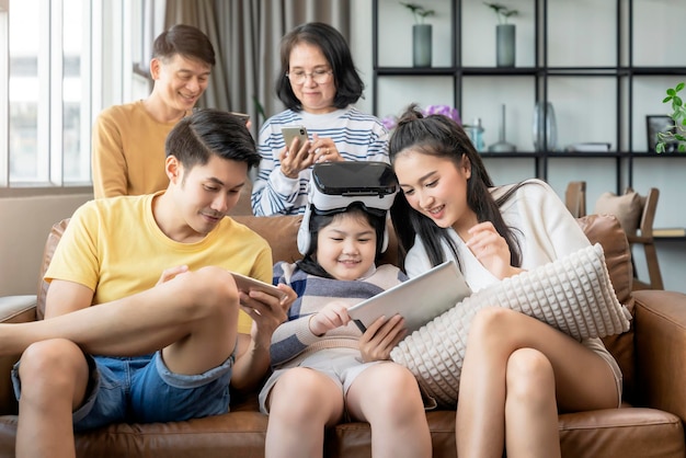 Tecnología inteligente con estilo de vida en el hogar. La familia de la generación asiática disfruta del dispositivo de tecnología. Usa la tableta del teléfono inteligente y las gafas de gafas vr para divertirse juntos en el sofá de la sala de estar en el momento de cuarentena en casa.