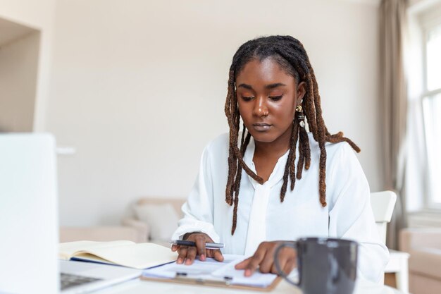 Tecnología de trabajo remoto y concepto de personas feliz sonriente joven mujer de negocios negra con computadora portátil y papeles trabajando en la oficina en casa