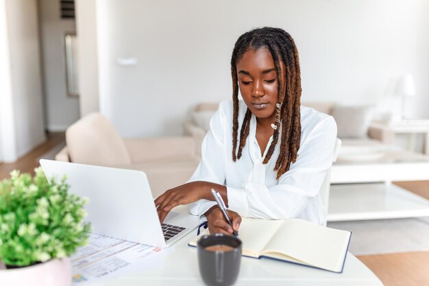 Tecnología de trabajo remoto y concepto de personas joven mujer de negocios africana con computadora portátil y papeles que trabajan en la oficina en casa durante la crisis de salud de Covid19