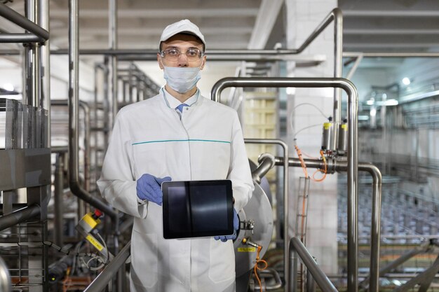 El tecnólogo de bata blanca con una tableta en las manos está en la tienda para la producción de mantequilla y queso El proceso de producción en la planta de productos lácteos Un lugar para una etiqueta
