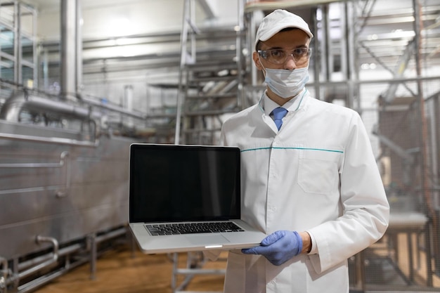 El tecnólogo con una computadora portátil en las manos prepara la línea de producción mientras se encuentra en el departamento de la fábrica de productos lácteos