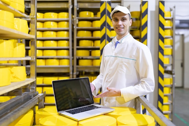 El tecnólogo con una computadora portátil en las manos prepara la línea de producción mientras se encuentra en el departamento de la fábrica de productos lácteos