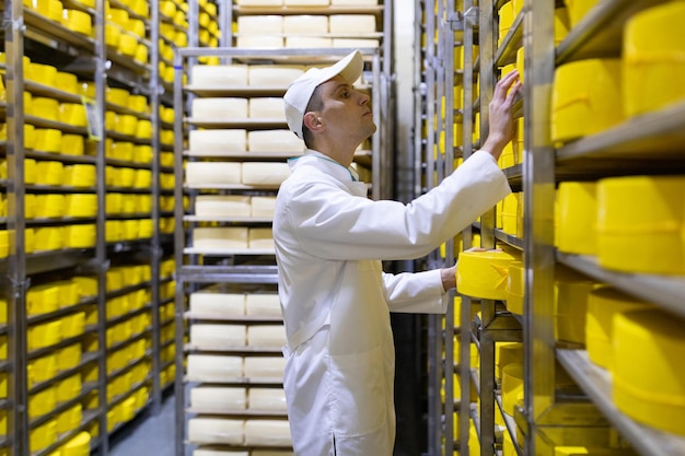 El tecnólogo con queso en las manos realiza una inspección de la producción lista en el departamento de la fábrica de productos lácteos