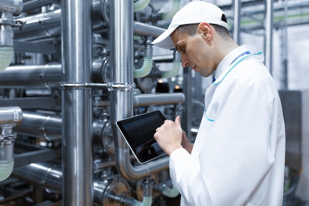 Foto gratuita el tecnólogo con una tableta gris en las manos prepara la línea de producción mientras se encuentra en el departamento de la fábrica de productos lácteos