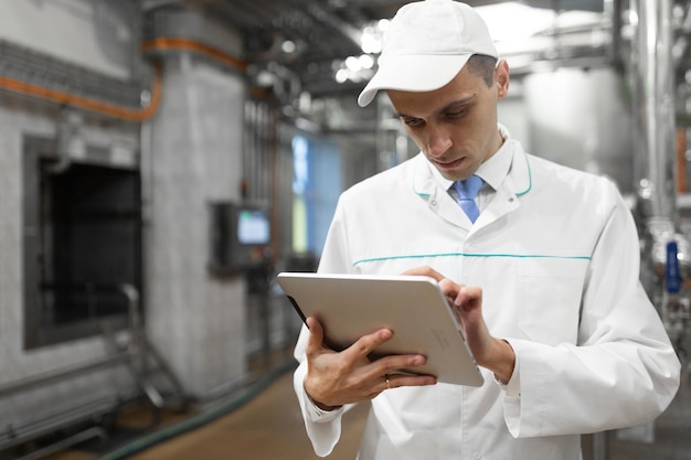El tecnólogo con una tableta gris en las manos prepara la línea de producción mientras se encuentra en el departamento de la fábrica de productos lácteos