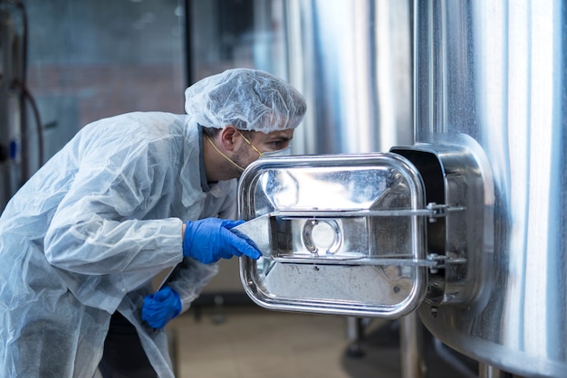 Foto gratuita tecnólogo en traje blanco mirando dentro de la máquina en la línea de producción de la fábrica de alimentos