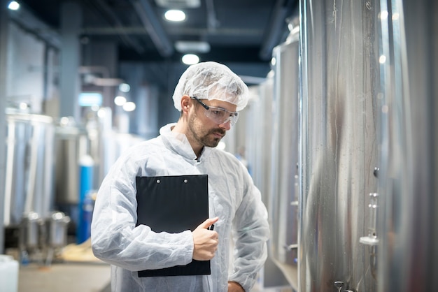 Tecnólogo en uniforme protector blanco de pie en la planta de la industria