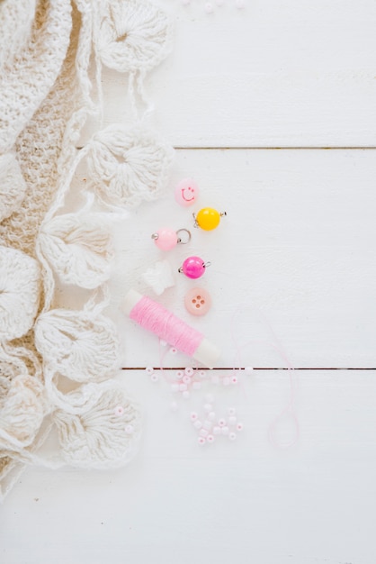 Tejido de ganchillo blanco; Perlas y carrete rosa en escritorio de madera