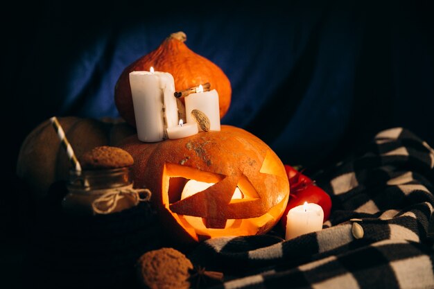 La tela escocesa miente alrededor Pumpking de Halloween con velas brillantes alrededor de ella y una taza de chocolate caliente con las galletas